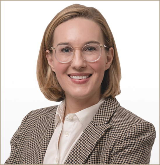 Emily Sheeren, smiling with arms crossed, wearing glasses and a houndstooth blazer